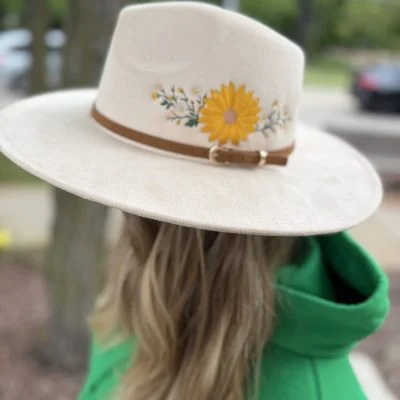 Cream wide brim suede fedora with a sunflower embroidered on the side, worn outdoors